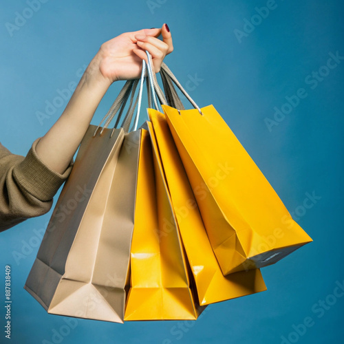 A hand holding several brown paper shopping bags against a bright background symbolizes shopping, sustainability and minimalist consumerism