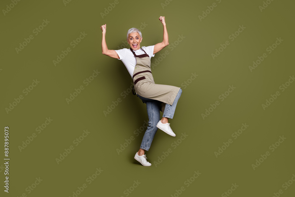 Full length photo of lucky positive woman wear apron serving coffee rising fists empty space isolated khaki color background Full length photo of lucky positive woman wear apron serving coffee rising fists empty space isolated khaki color background