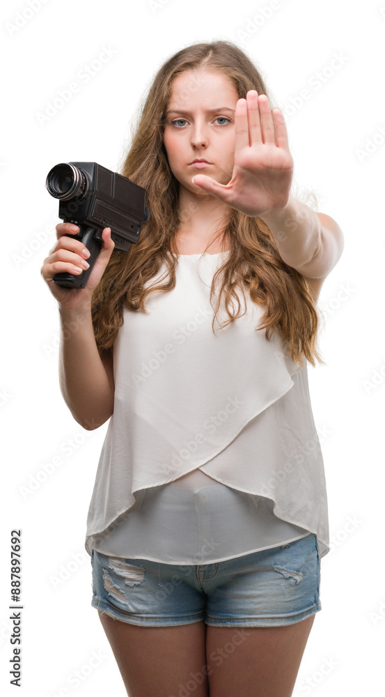 Young blonde woman holding super 8 video camera with open hand doing stop sign with serious and confident expression, defense gesture Young blonde woman holding super 8 video camera with open hand doing stop sign with serious and confident expression, defense gesture