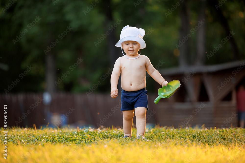 Happy little boy running and play in park on grass with shovel, sunlight. Concept lifestyle childhood moment Happy little boy running and play in park on grass with shovel, sunlight. Concept lifestyle childhood moment