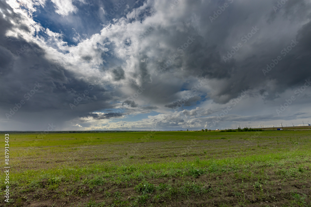 A vast green field stretches out beneath a sky filled with dramatic, dark clouds. The clouds are illuminated from behind, creating a sense of impending rain.. A vast green field stretches out beneath a sky filled with dramatic, dark clouds. The clouds are illuminated from behind, creating a sense of impending rain..