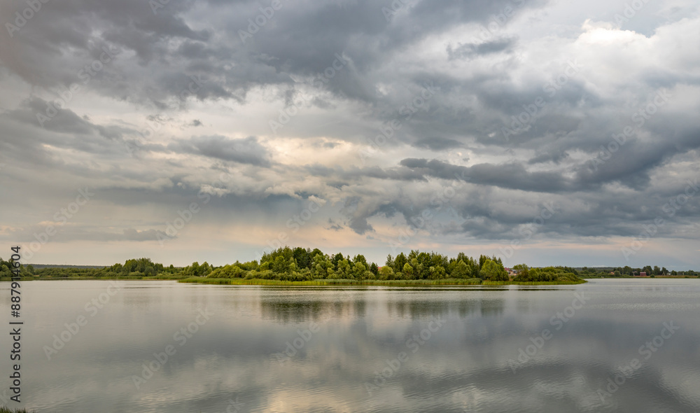 A tranquil scene of a small, forested island in a still lake, framed by a vast expanse of dramatic, grey clouds in the summer sky. A tranquil scene of a small, forested island in a still lake, framed by a vast expanse of dramatic, grey clouds in the summer sky.