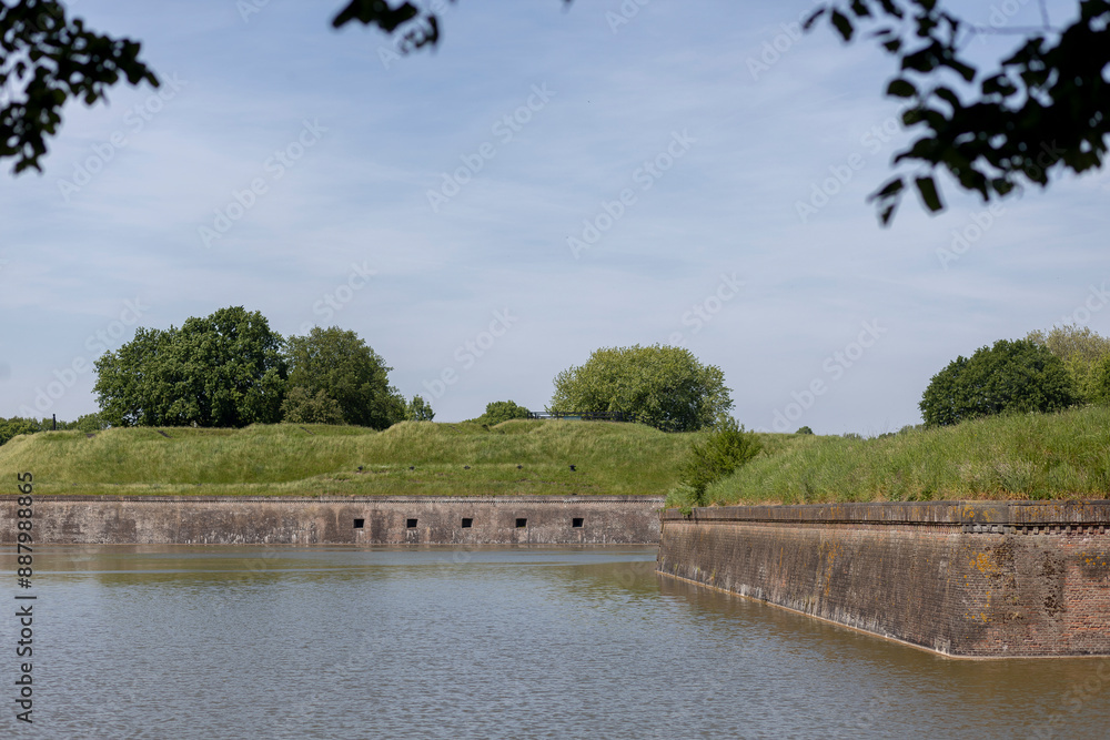 Greenery with church tower on top and behind Naarden Vesting moated Dutch stronghold city with defense structure bastion walls with canal in front Greenery with church tower on top and behind Naarden Vesting moated Dutch stronghold city with defense structure bastion walls with canal in front
