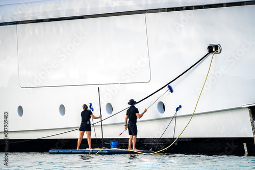 Super yacht crew, two deckhands, male and female cleaning the side of a white mega at dock in English Harbour, a famous caribbean island of Antigua know for yacht season photo