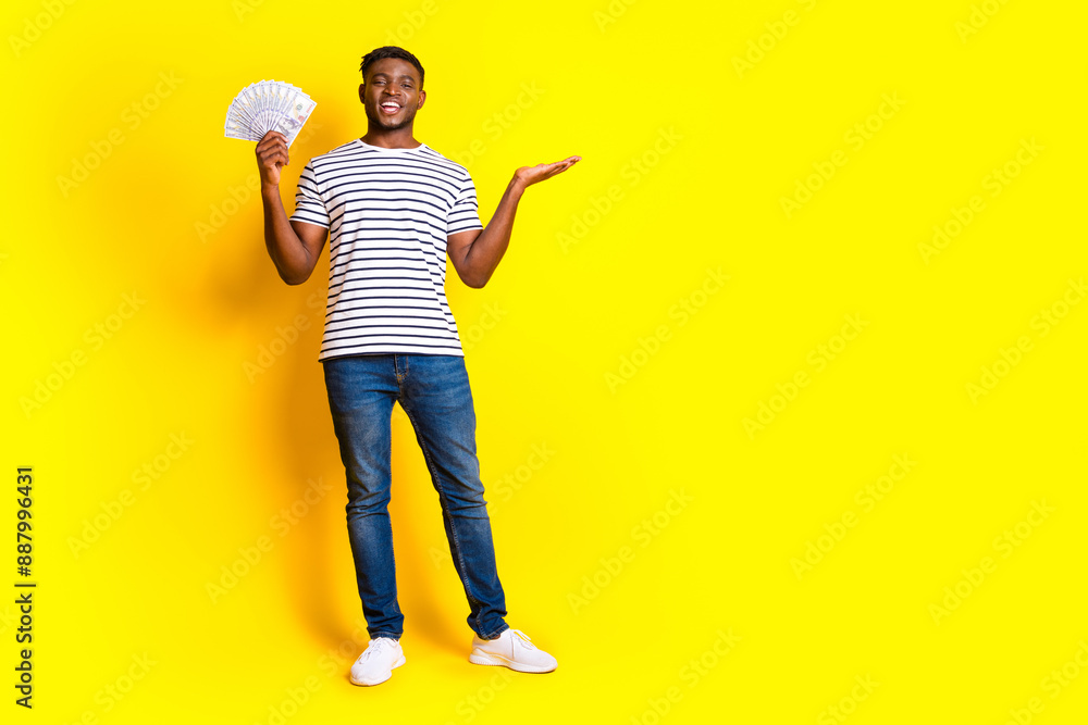Full size photo of nice young man hold bills empty space wear t-shirt isolated on bright yellow color background Full size photo of nice young man hold bills empty space wear t-shirt isolated on bright yellow color background
