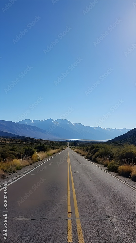 Long straight road leading through a scenic valley with mountain ranges in the distance under a clear blue sky. Long straight road leading through a scenic valley with mountain ranges in the distance under a clear blue sky.