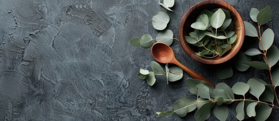 Top view of eucalyptus leaves next to a wooden bowl and spoon with copy space image