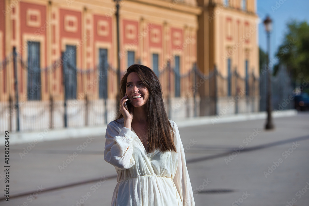 Fototapeta premium Young and beautiful Latin woman talking on mobile phone is having fun and is happy and smiling loudly. The woman is on the street and walks through the city. Concept communications.