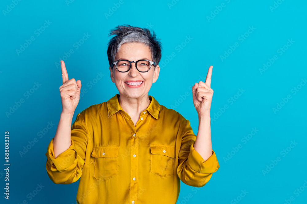 Photo of pretty cheerful woman wear blouse spectacles showing fingers up emtpy space isolated blue color background Photo of pretty cheerful woman wear blouse spectacles showing fingers up emtpy space isolated blue color background