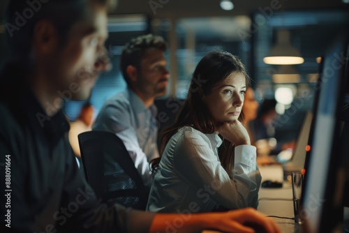 Late night at the office. Team working overtime, woman looks tired but focused. Dim lighting adds to tense atmosphere. photo