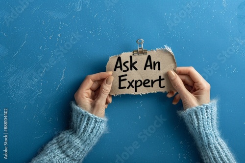 Expert Consulting Concept with Hands Holding 'Ask An Expert' Sign on Blue Background