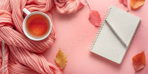 Feminine flat lay background with cup of tea, cozy sweater, notebook and autumnal leaves on a pastel pink background. Great design with copy space.