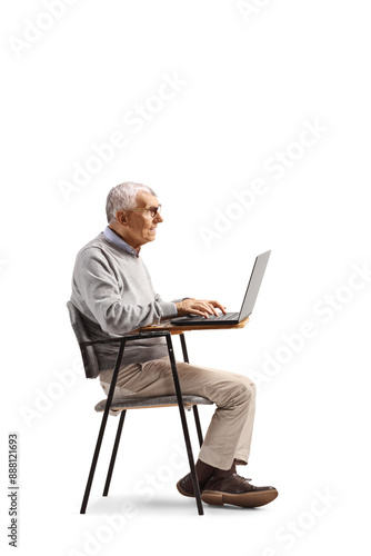 Elderly man sitting in a school chair and using a laptop computer