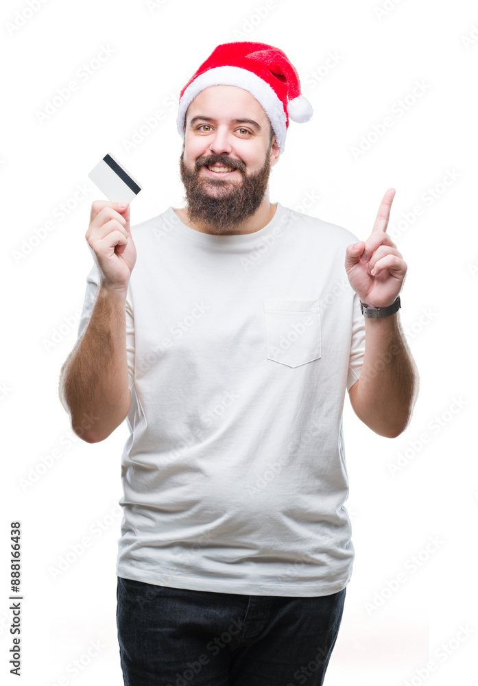 Young caucasian man wearing christmas hat holding credit card over isolated background surprised with an idea or question pointing finger with happy face, number one Young caucasian man wearing christmas hat holding credit card over isolated background surprised with an idea or question pointing finger with happy face, number one