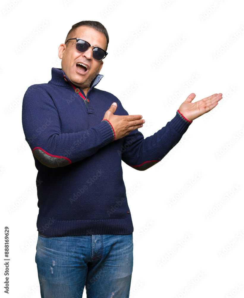 Fototapeta premium Middle age arab man wearing sunglasses over isolated background amazed and smiling to the camera while presenting with hand and pointing with finger.