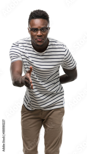 Young african american man wearing glasses and navy t-shirt smiling friendly offering handshake as greeting and welcoming. Successful business.