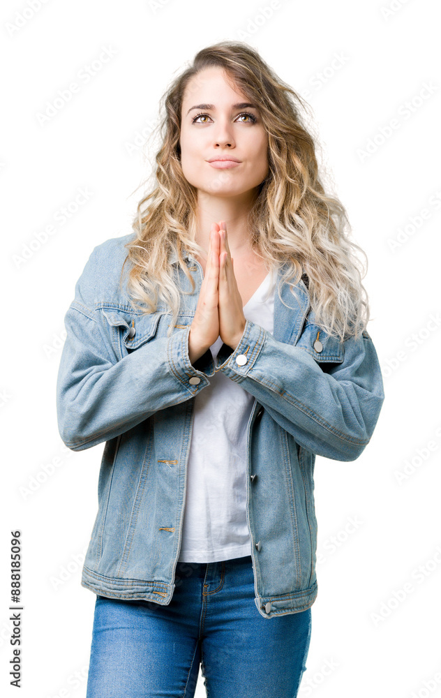 Beautiful young blonde woman wearing denim jacket over isolated background praying with hands together asking for forgiveness smiling confident. Beautiful young blonde woman wearing denim jacket over isolated background praying with hands together asking for forgiveness smiling confident.