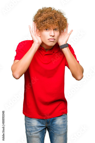 Young handsome man with afro hair wearing red t-shirt Trying to hear both hands on ear gesture, curious for gossip. Hearing problem, deaf