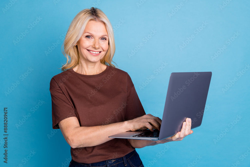 Photo of adorable lovely pensioner woman wear brown clothes use netbook isolated on blue color background Photo of adorable lovely pensioner woman wear brown clothes use netbook isolated on blue color background