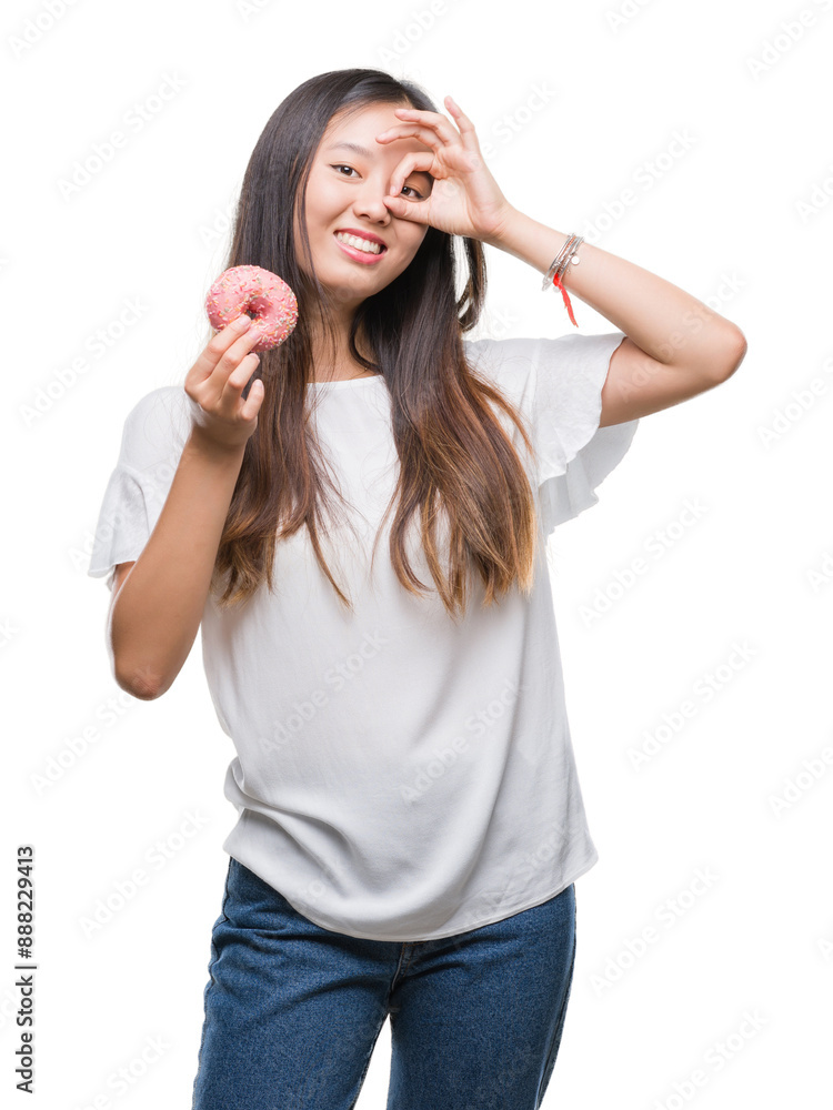 Young asian woman eating donut over isolated background with happy face smiling doing ok sign with hand on eye looking through fingers Young asian woman eating donut over isolated background with happy face smiling doing ok sign with hand on eye looking through fingers