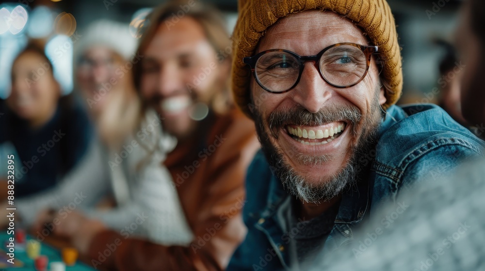 A cheerful man in a hat and glasses laughs heartily with friends at an indoor gathering, spreading joy and camaraderie in a warmly lit and friendly environment. A cheerful man in a hat and glasses laughs heartily with friends at an indoor gathering, spreading joy and camaraderie in a warmly lit and friendly environment.