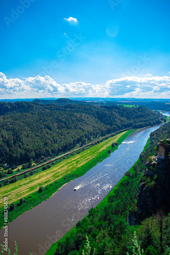 a narrow river flows in the mountains, many green trees, blue sky, clouds photo