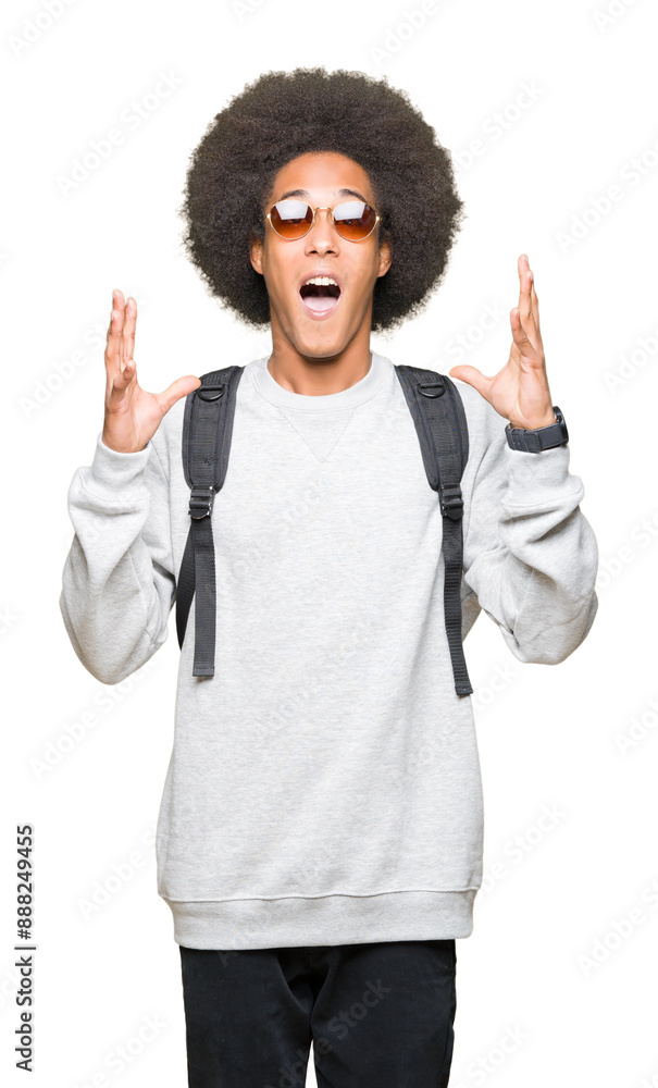 Young african american man with afro hair wearing sunglasses and backpack very happy and excited, winner expression celebrating victory screaming with big smile and raised hands Young african american man with afro hair wearing sunglasses and backpack very happy and excited, winner expression celebrating victory screaming with big smile and raised hands