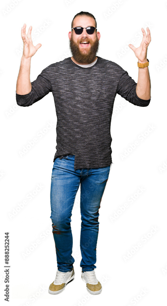Naklejka premium Young hipster man wearing sunglasses celebrating crazy and amazed for success with arms raised and open eyes screaming excited. Winner concept