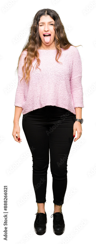 Obraz premium Young beautiful woman wearing pink sweater sticking tongue out happy with funny expression. Emotion concept.