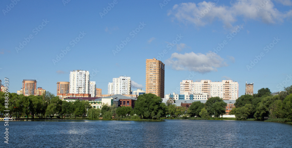 Beautiful panoramic landscape - modern high-rise buildings on the shore of a pond among the lush foliage of trees in Reutov, Moscow region on a clear summer sunny day Beautiful panoramic landscape - modern high-rise buildings on the shore of a pond among the lush foliage of trees in Reutov, Moscow region on a clear summer sunny day