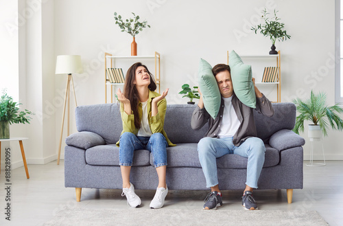 Anxious couple at home, man covering ears with pillow, unhappy irritated family ignoring loud noise sound, feeling stressed of noisy disturbing neighbors, loud music, hating hearing sound of works  photo