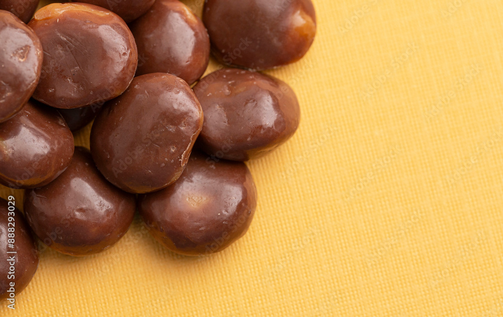 Sweet Chocolate Covered Caramel Disks on Yellow Background Sweet Chocolate Covered Caramel Disks on Yellow Background