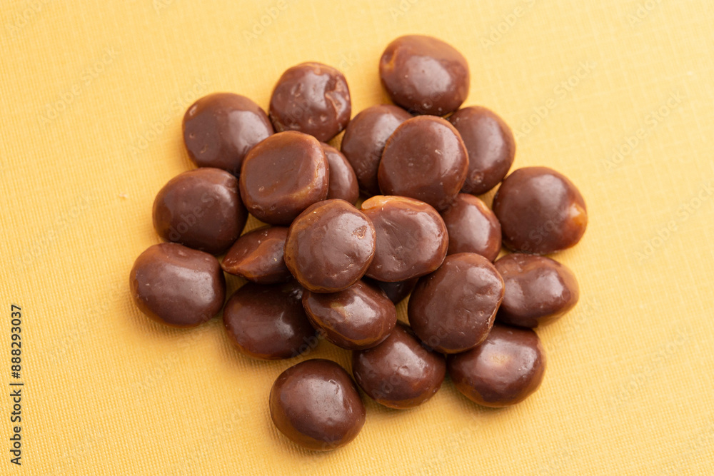 Sweet Chocolate Covered Caramel Disks on Yellow Background Sweet Chocolate Covered Caramel Disks on Yellow Background