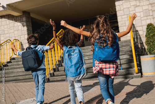 Φωτογραφία Group of happy multiracial schoolmates elementary middle school kids pupils walking to school together running hurrying to the building for classes lessons