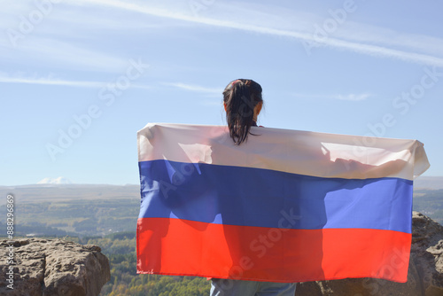 Obraz na płótnie The Russian flag is on the shoulders of a girl standing against the backdrop of the Caucasus mountains. Unity Day in Russia. w salonie