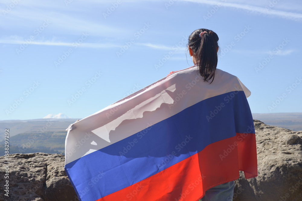 The Russian flag is on the shoulders of a girl standing against the backdrop of the Caucasus mountains. Unity Day in Russia.