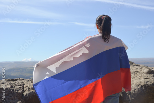 Obraz na płótnie The Russian flag is on the shoulders of a girl standing against the backdrop of the Caucasus mountains. Unity Day in Russia. w salonie