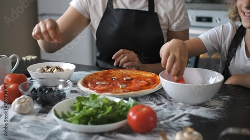 Wallpaper Mural In cozy kitchen, a mother is placing slices of mushrooms onto a pizza crust topped with sauce, while her daughter adds fresh tomato slices. Slow motion. Family collaboration and healthy cooking Torontodigital.ca