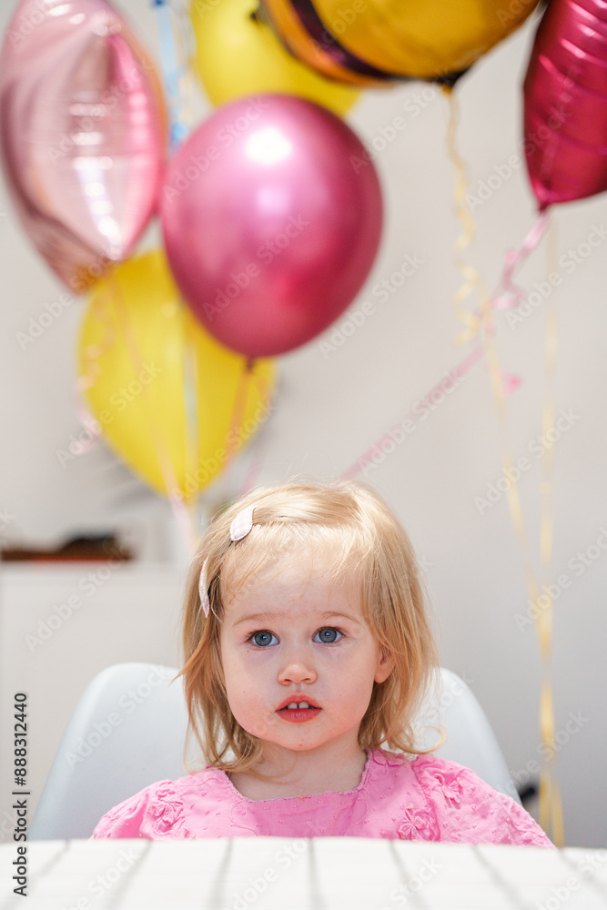 A cute Caucasian toddler girl is sitting at a festive table and waiting for guests. A cute Caucasian toddler girl is sitting at a festive table and waiting for guests.