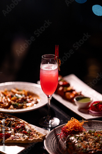 Red cocktail drink in glass on dark background with foods on table. Pizza, Pasta and Kebab platter with Cocktail.