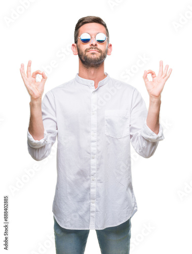 Young handsome man wearing glasses over isolated background relax and smiling with eyes closed doing meditation gesture with fingers. Yoga concept.