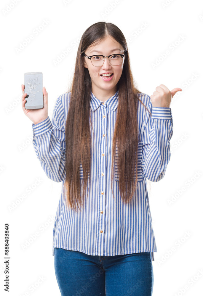 Obraz premium Young Chinese woman over isolated background showing broken smartphone screen pointing and showing with thumb up to the side with happy face smiling