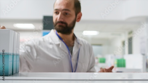 POV of pharmacist taking medicaments from drugstore shelves, working on reorganizing remedies and supplements in a pharmacy. Male worker emptying racks of vitamins and treatments. Tripod shot.