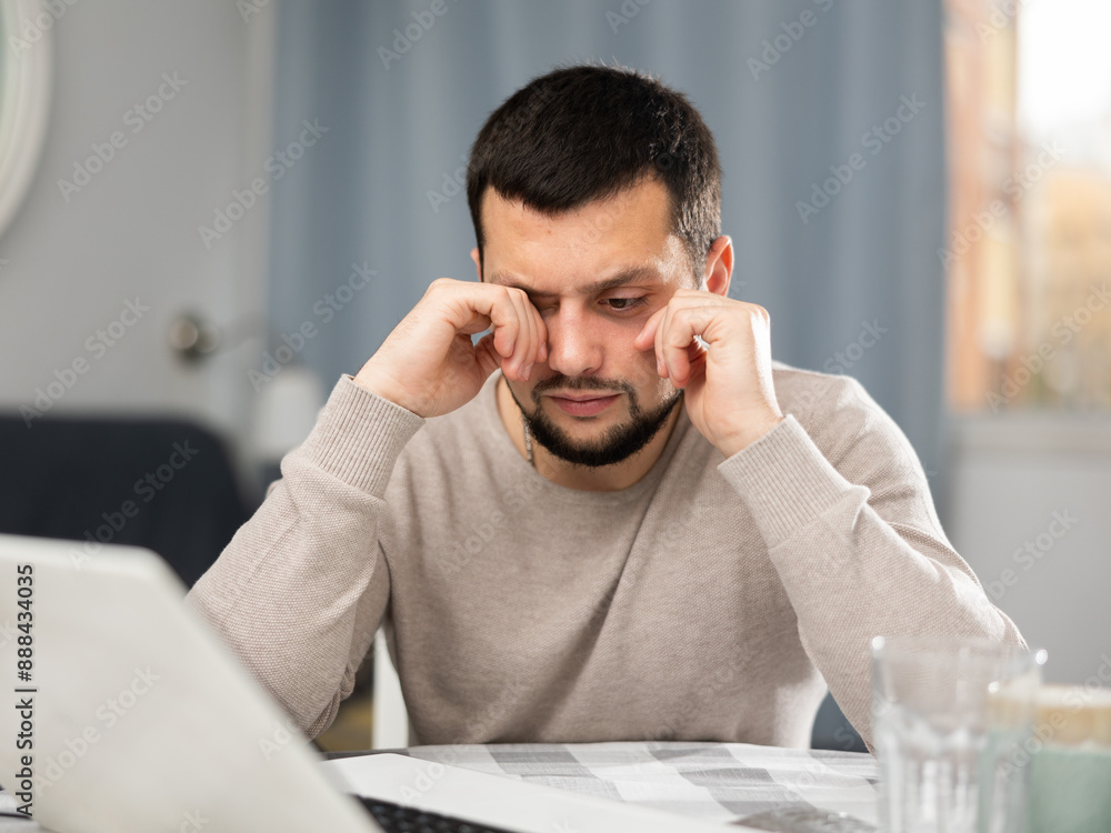 Naklejka premium Man rubs tired eyes with his hands after a long work at a laptop at home