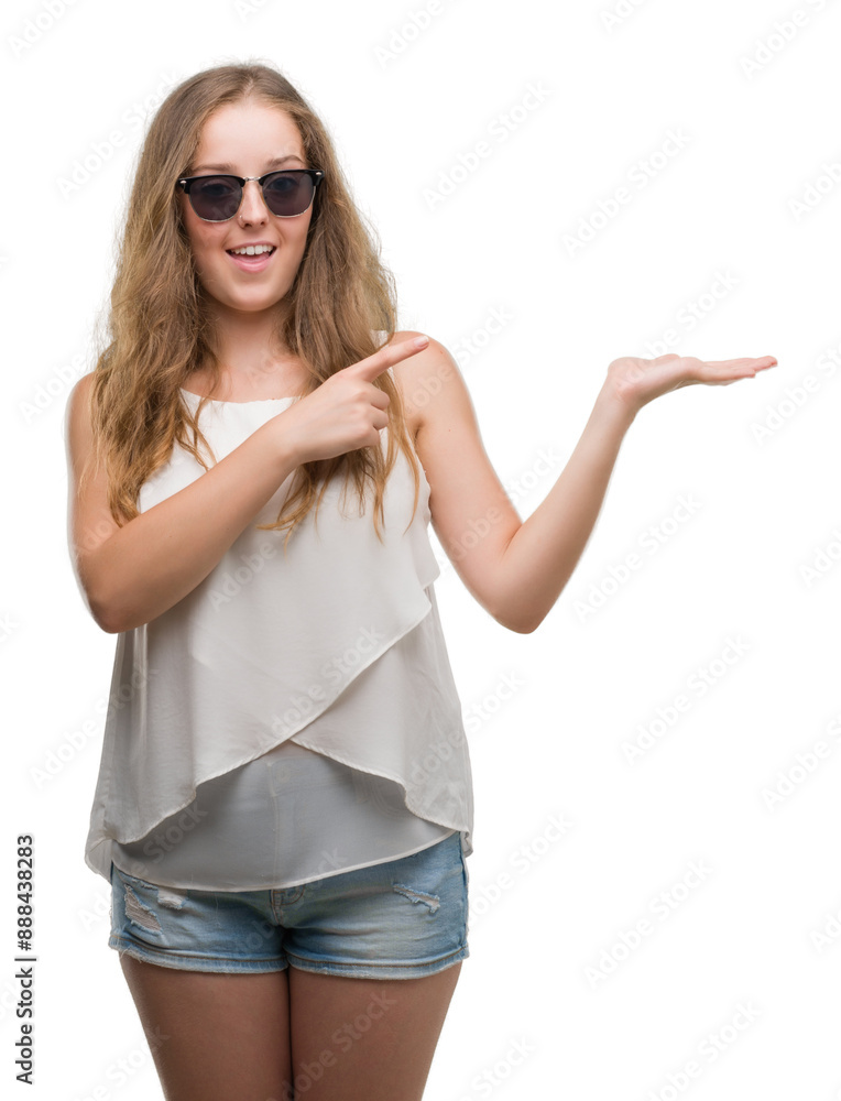 Young blonde woman wearing sunglasses amazed and smiling to the camera while presenting with hand and pointing with finger. Young blonde woman wearing sunglasses amazed and smiling to the camera while presenting with hand and pointing with finger.