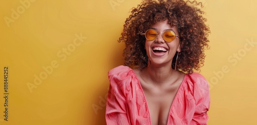 Woman With Curly Hair Laughing In Sunglasses Against Yellow Wall