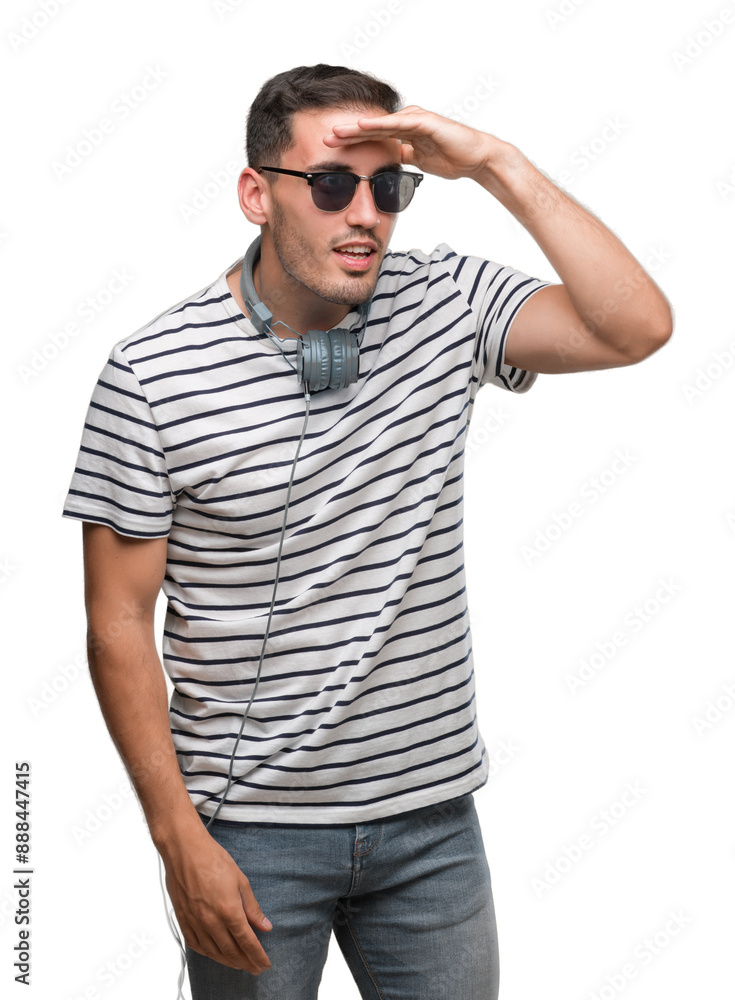 Handsome young man wearing headphones very happy and smiling looking far away with hand over head. Searching concept. Handsome young man wearing headphones very happy and smiling looking far away with hand over head. Searching concept.