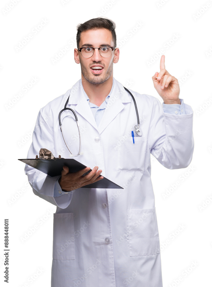 Handsome young doctor man holding a clipboard surprised with an idea or question pointing finger with happy face, number one Handsome young doctor man holding a clipboard surprised with an idea or question pointing finger with happy face, number one