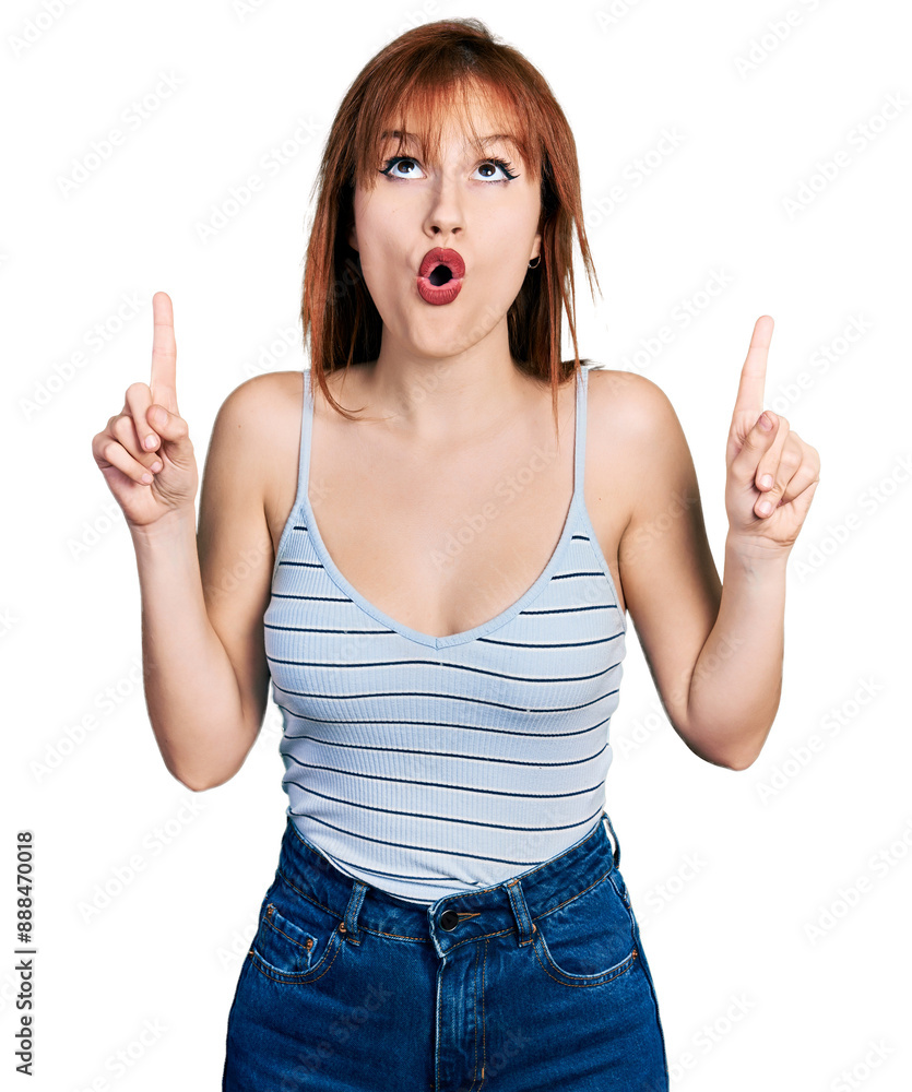 Redhead young woman wearing casual style with sleeveless shirt amazed and surprised looking up and pointing with fingers and raised arms. Redhead young woman wearing casual style with sleeveless shirt amazed and surprised looking up and pointing with fingers and raised arms.