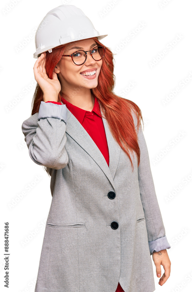 Young redhead woman wearing architect hardhat smiling with hand over ear listening an hearing to rumor or gossip. deafness concept. Young redhead woman wearing architect hardhat smiling with hand over ear listening an hearing to rumor or gossip. deafness concept.